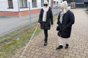 Zwei Frauen laufen einen Weg entlang, eine davon trägt eine Augenmaske.